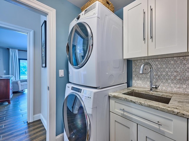 laundry area featuring dark hardwood / wood-style flooring, stacked washer / drying machine, cabinets, and sink