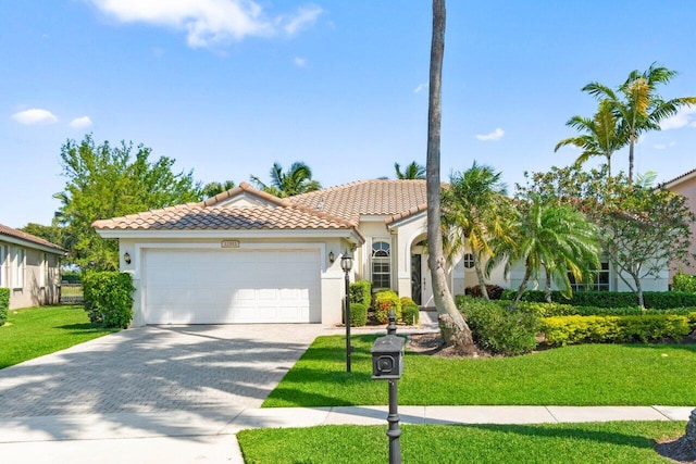 mediterranean / spanish home featuring a garage, a tile roof, driveway, stucco siding, and a front yard