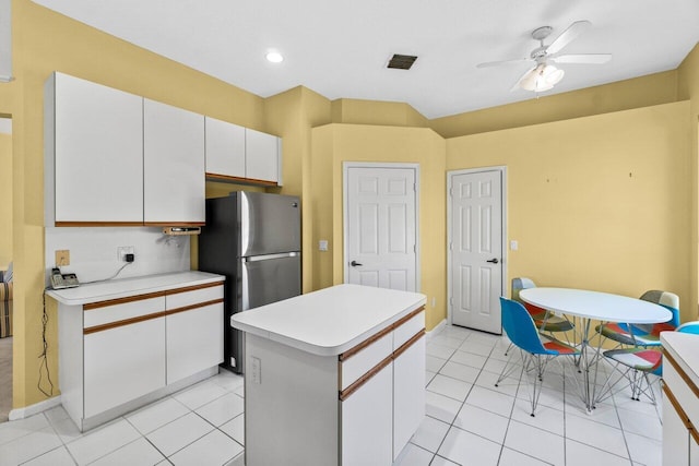 kitchen with light countertops, a kitchen island, freestanding refrigerator, and white cabinetry