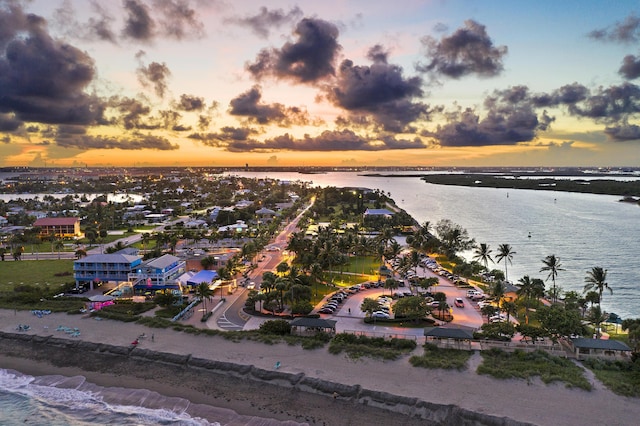 aerial view at dusk featuring a water view and a view of the beach