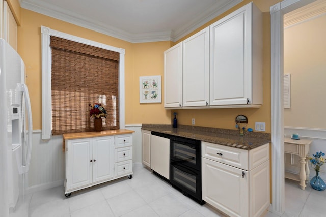 bar featuring light tile patterned floors, crown molding, white refrigerator with ice dispenser, and a wainscoted wall