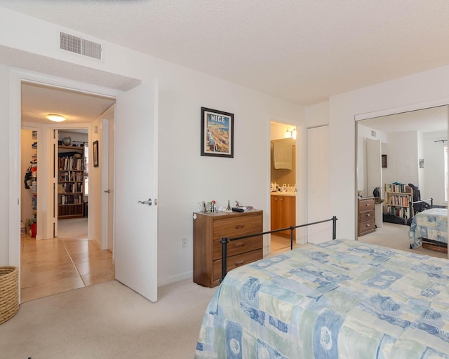 carpeted bedroom with ensuite bathroom, a closet, and a textured ceiling