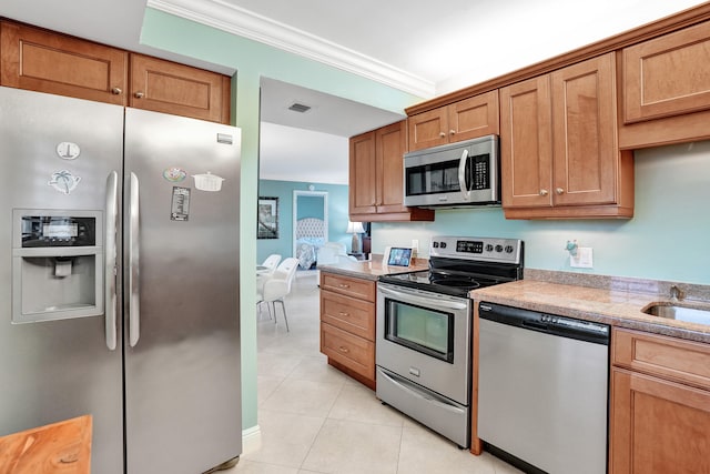 kitchen featuring light stone counters, light tile patterned floors, crown molding, and appliances with stainless steel finishes