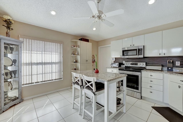 kitchen with light tile patterned floors, appliances with stainless steel finishes, white cabinetry, a kitchen breakfast bar, and a center island