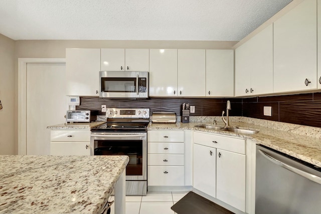 kitchen with stainless steel appliances, light stone countertops, sink, and white cabinets