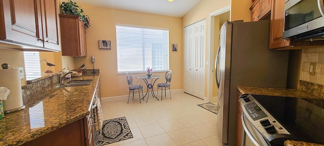 kitchen featuring light tile patterned flooring, appliances with stainless steel finishes, lofted ceiling, sink, and dark stone counters