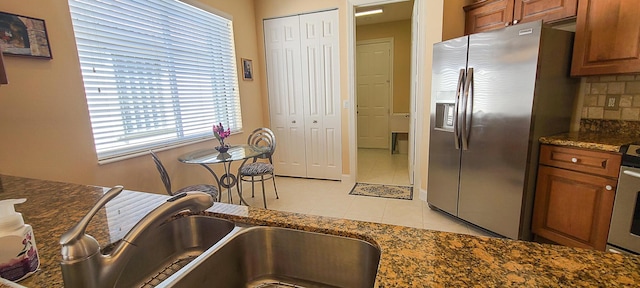 kitchen featuring sink, dark stone countertops, light tile patterned floors, stainless steel fridge, and decorative backsplash