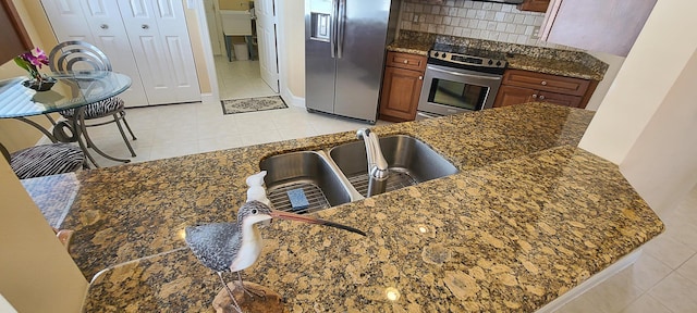 kitchen with tasteful backsplash, light tile patterned floors, appliances with stainless steel finishes, kitchen peninsula, and dark stone counters