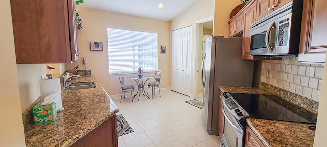 kitchen with lofted ceiling, sink, light tile patterned floors, dark stone countertops, and stainless steel appliances