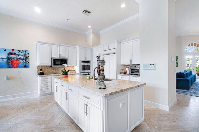 kitchen with built in microwave, an island with sink, sink, white cabinets, and backsplash