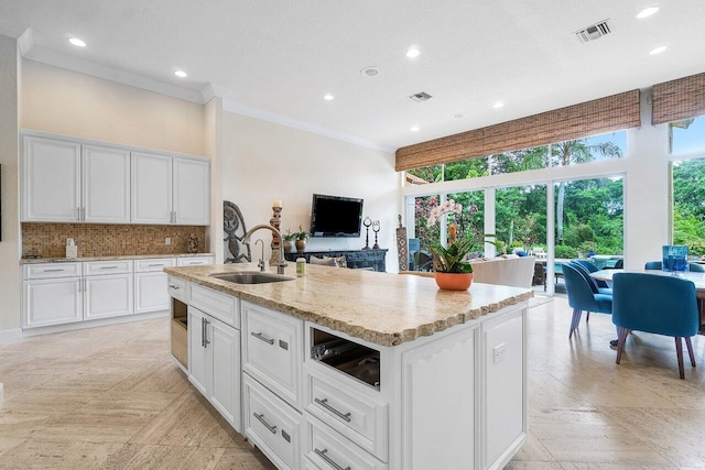 kitchen featuring white cabinetry, sink, decorative backsplash, and a center island with sink