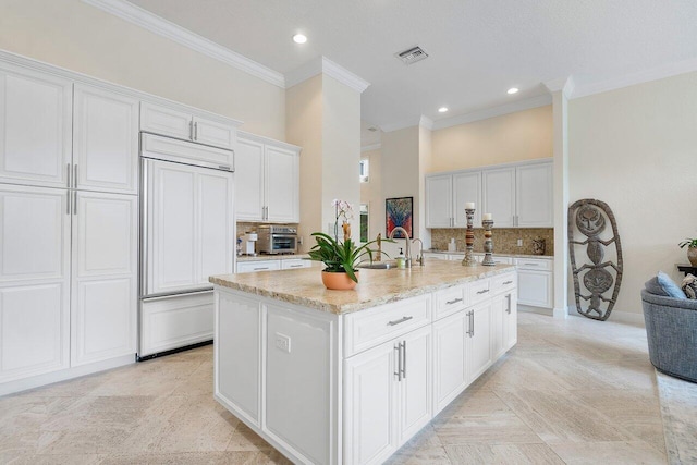 kitchen featuring white cabinetry, paneled fridge, a center island with sink, and backsplash