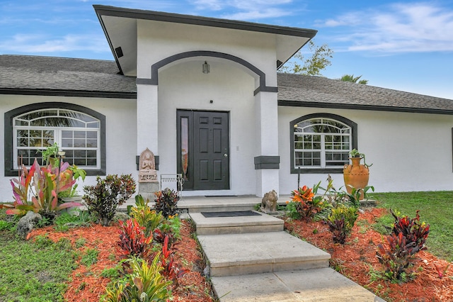 entrance to property featuring a shingled roof and stucco siding