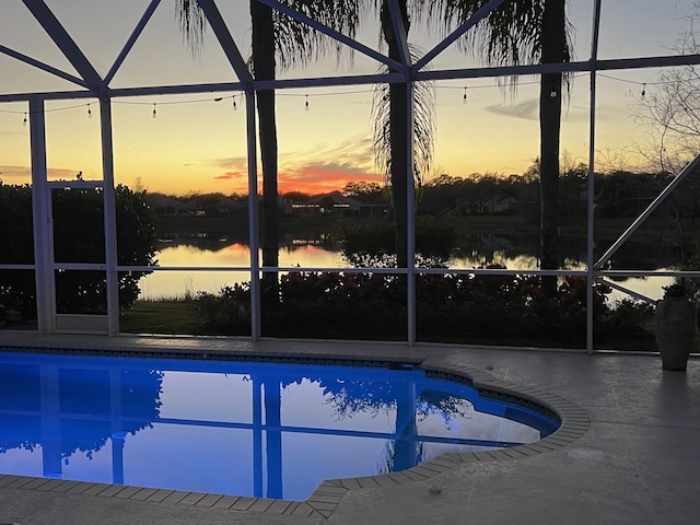 pool at dusk with a water view, glass enclosure, and a patio area