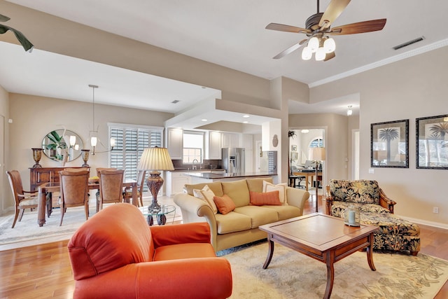 living room featuring ornamental molding, sink, ceiling fan with notable chandelier, and light hardwood / wood-style flooring