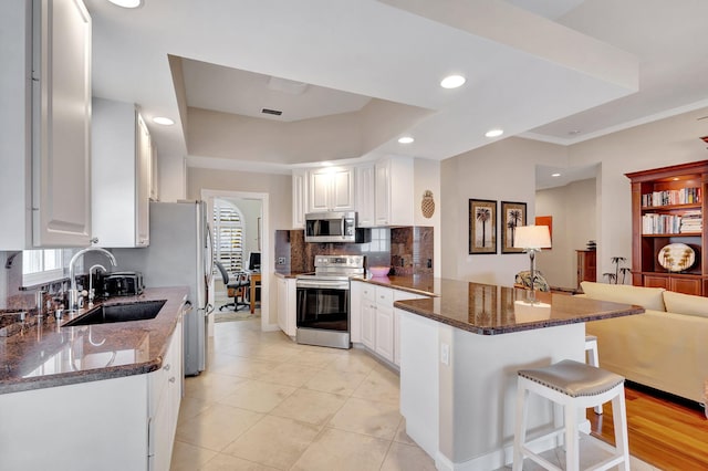 kitchen featuring backsplash, appliances with stainless steel finishes, a sink, a peninsula, and a kitchen bar