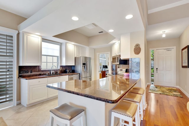 kitchen featuring appliances with stainless steel finishes, a kitchen bar, kitchen peninsula, and white cabinets