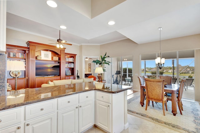 kitchen with dark stone counters, a wealth of natural light, ceiling fan with notable chandelier, and white cabinetry