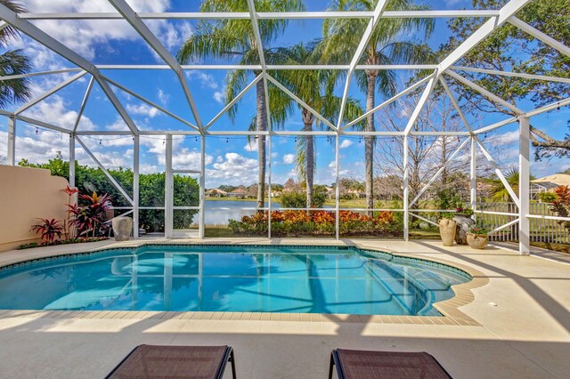 pool at dusk featuring a water view, a lanai, and a patio