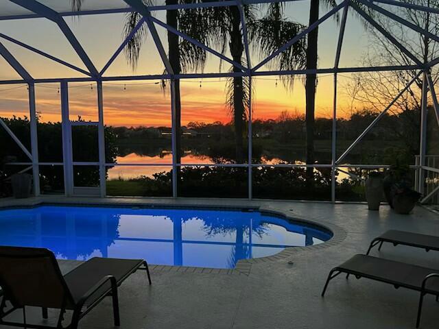 pool at dusk featuring a lanai, an outdoor pool, and a patio