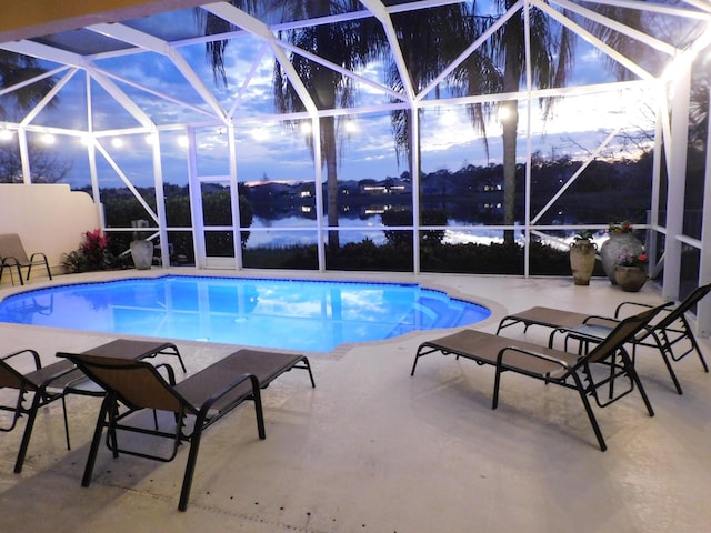 pool at dusk with a patio, a water view, and glass enclosure