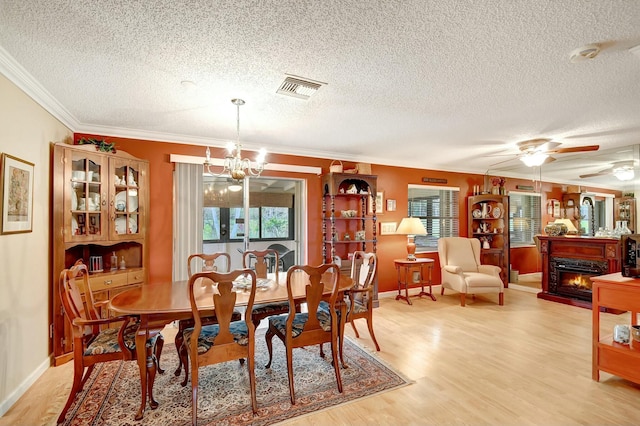 dining room with visible vents, ceiling fan with notable chandelier, light wood-style floors, a lit fireplace, and crown molding