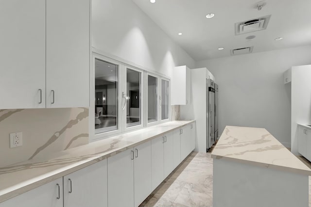 kitchen with visible vents, marble finish floor, a center island, white cabinetry, and light stone countertops