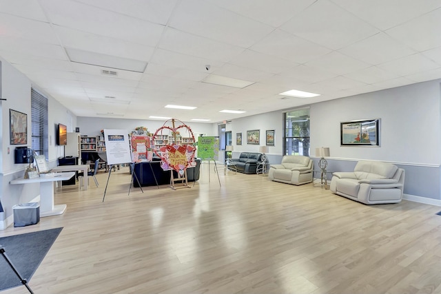 living area featuring visible vents, light wood-type flooring, a drop ceiling, and baseboards