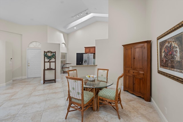 tiled dining area featuring track lighting, high vaulted ceiling, and a skylight