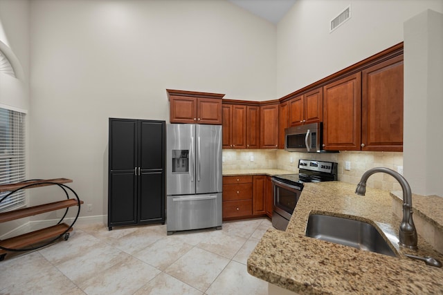 kitchen featuring a towering ceiling, sink, decorative backsplash, stainless steel appliances, and light stone countertops