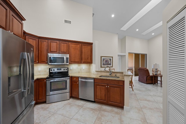 kitchen featuring sink, light tile patterned floors, stainless steel appliances, a high ceiling, and light stone counters