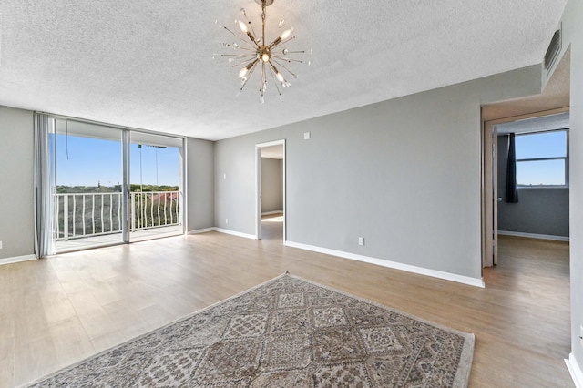 unfurnished room featuring floor to ceiling windows, a chandelier, a textured ceiling, and light wood-type flooring