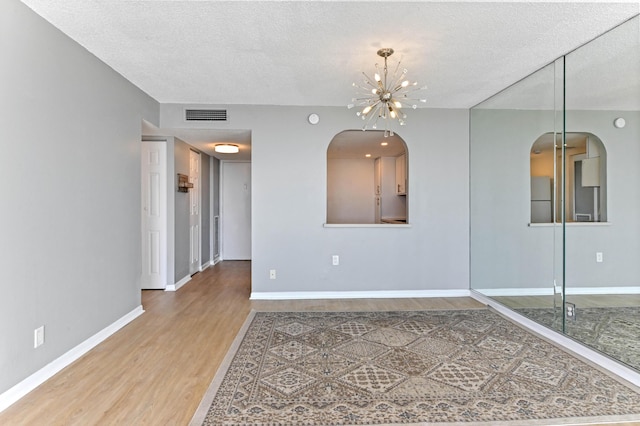 empty room featuring hardwood / wood-style floors, a textured ceiling, and a chandelier