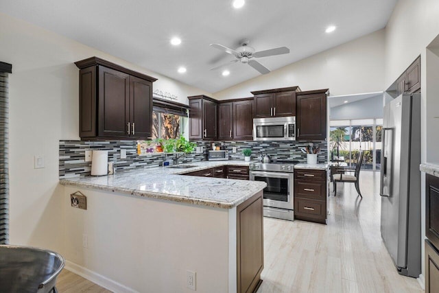 kitchen with lofted ceiling, sink, light stone counters, appliances with stainless steel finishes, and kitchen peninsula