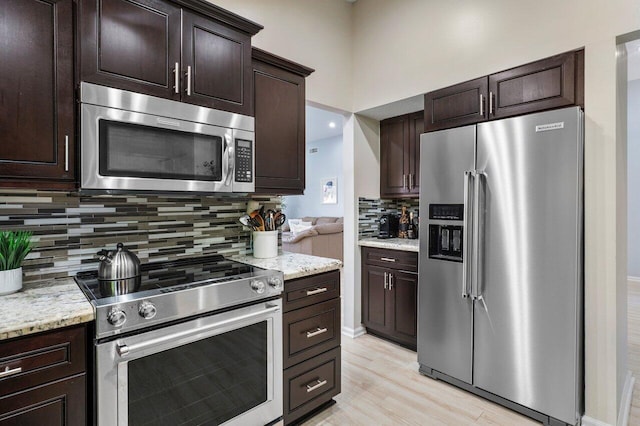 kitchen with stainless steel appliances, light stone countertops, dark brown cabinets, and backsplash