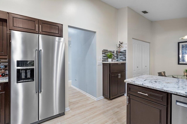 kitchen featuring light stone countertops, appliances with stainless steel finishes, dark brown cabinets, and light wood-type flooring