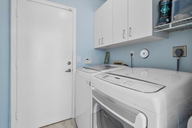 laundry room with light hardwood / wood-style floors, washing machine and dryer, and cabinets