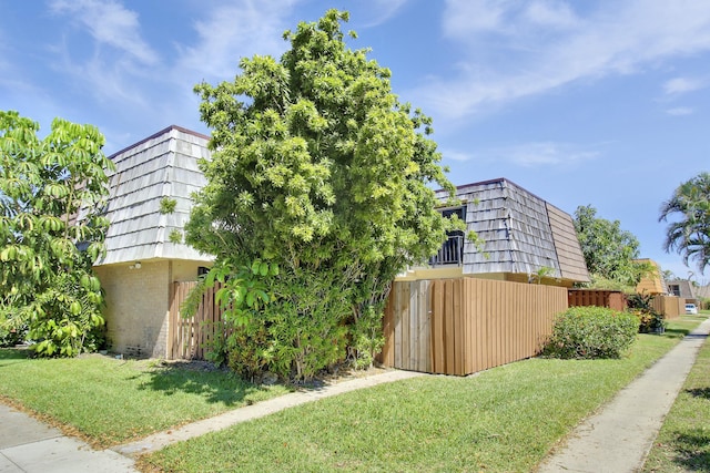 view of property exterior featuring mansard roof, a lawn, and fence