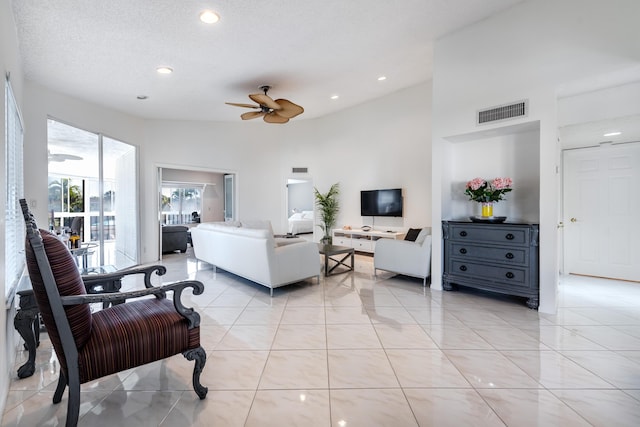 tiled living room featuring ceiling fan, a textured ceiling, and a high ceiling