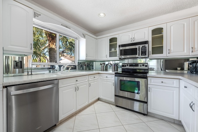 kitchen featuring sink, light tile patterned floors, stainless steel appliances, and white cabinets