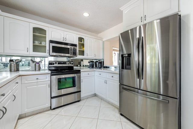 kitchen with light tile patterned floors, a textured ceiling, stainless steel appliances, and white cabinets