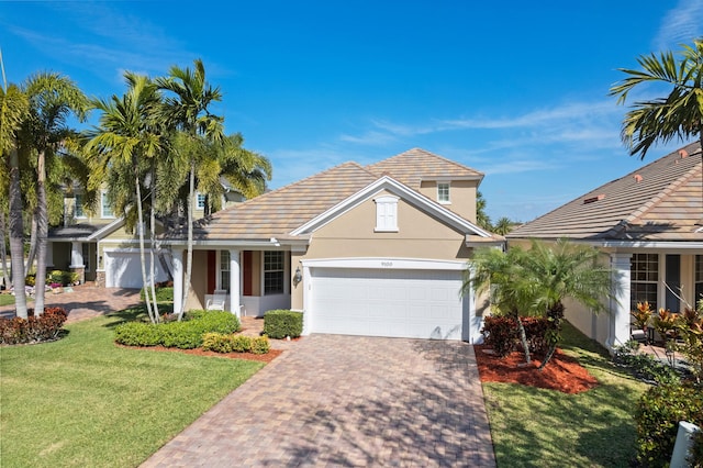 view of front of home with decorative driveway, a tile roof, stucco siding, a garage, and a front lawn