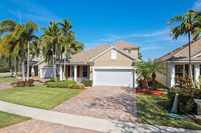 view of front of home featuring a tile roof, an attached garage, decorative driveway, a front lawn, and stucco siding