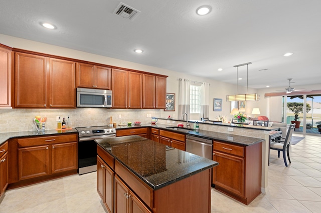 kitchen featuring decorative light fixtures, stainless steel appliances, visible vents, a sink, and a kitchen island