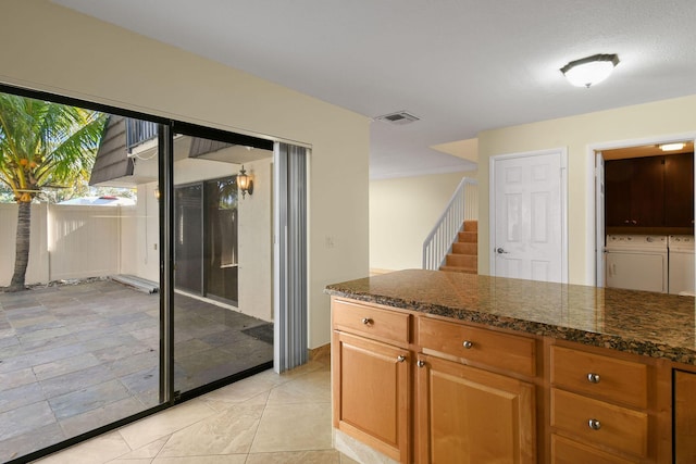 kitchen with light tile patterned floors, washing machine and dryer, and dark stone counters