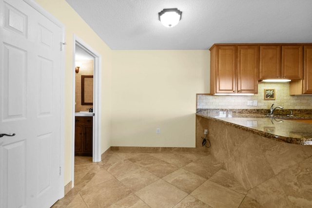 kitchen with tasteful backsplash, dark stone counters, sink, and a textured ceiling