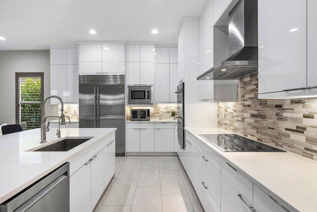 kitchen featuring sink, built in appliances, white cabinets, and wall chimney exhaust hood