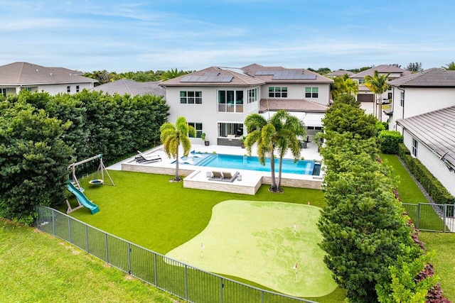 rear view of property featuring a fenced in pool, a lawn, a patio, a playground, and solar panels