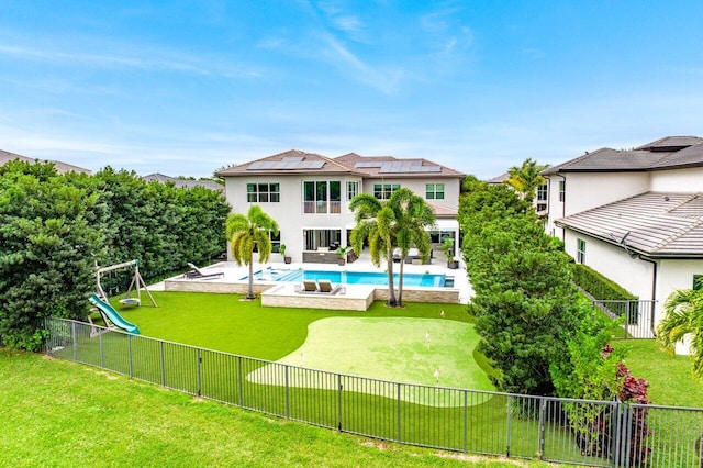 back of house featuring a playground, solar panels, a lawn, a fenced in pool, and a patio area