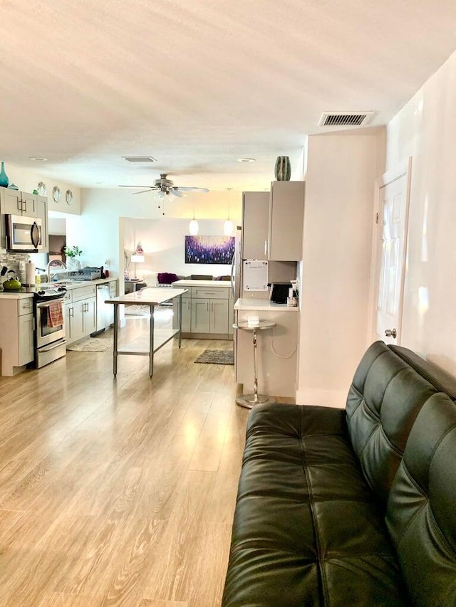 living room featuring ceiling fan, sink, and light wood-type flooring